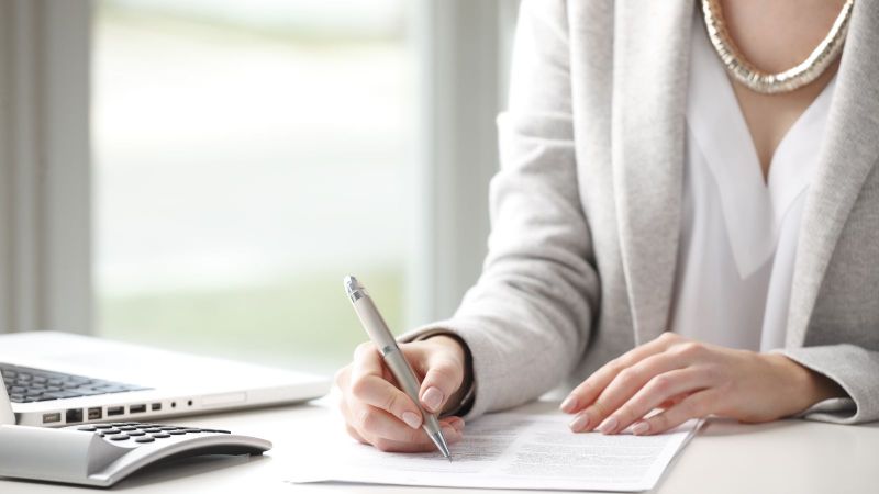 Das Bild zeigt eine Frau beim Unterzeichnen eines Dokumentes.