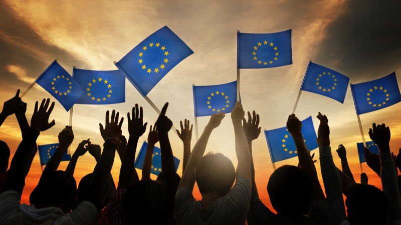 Das Bild zeigt eine Gruppe Menschen,  mit kleinen Europa-Flaggen in den Händen.