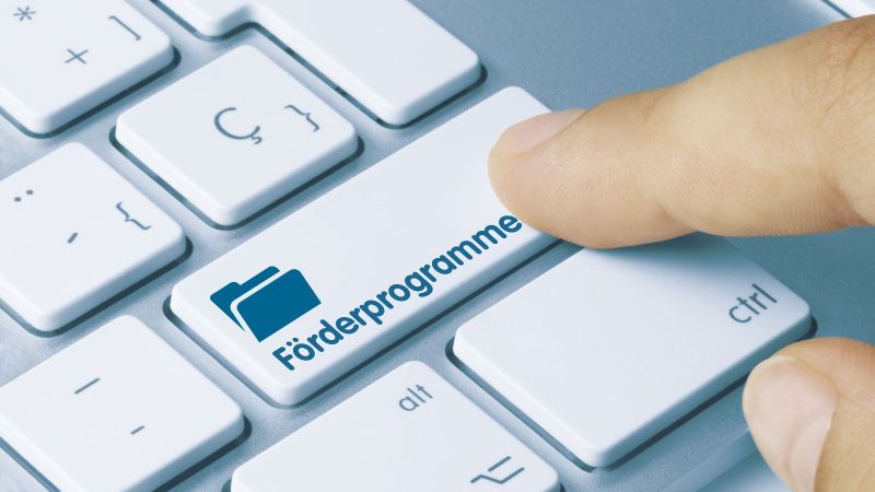 Computertastatur mit einem menschlichen Finger, der die Taste Förderprogramme anklickt