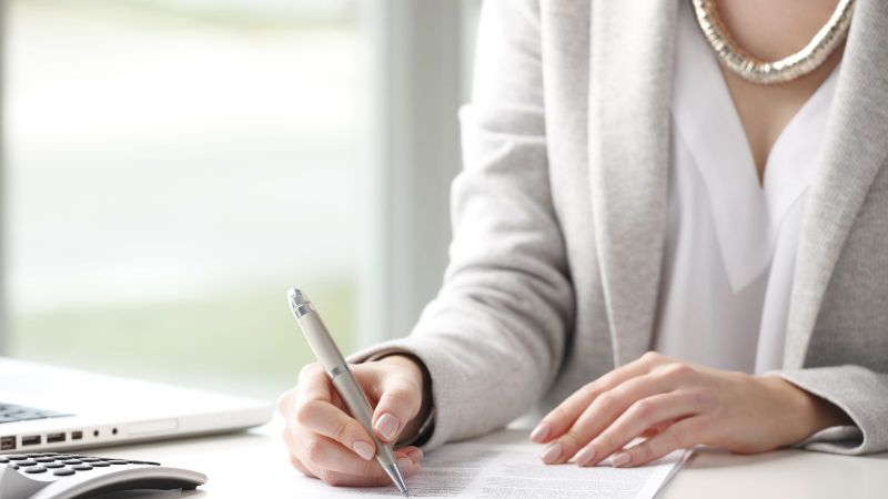 Das Bild zeigt eine Frau beim Unterzeichnen eines Dokumentes.