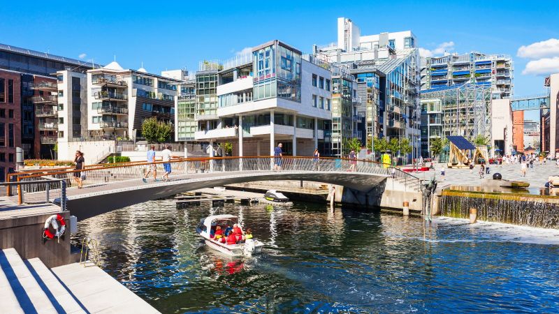 Das Bild zeigt einen Fluss in einer Stadt. Eine Brücke ist über dem Fluss zu sehen, auf der Menschen laufen.