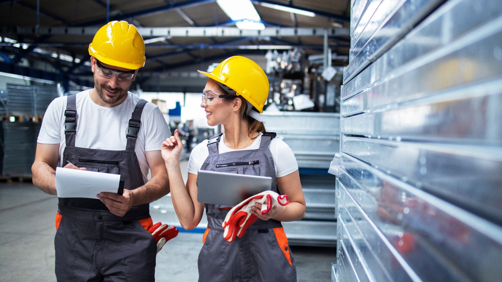 Das Bild zeigt arbeitende Fabrikarbeiter mit Helm im Gespräch.